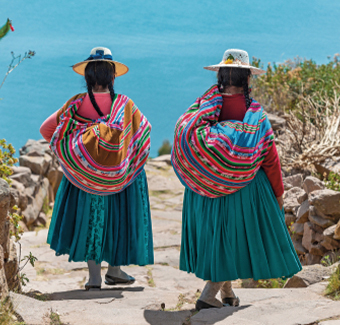 2 jeunes filles marchant face à la mer avec des tenues traditionnelles : jupe bleu, haut rose, tresses, chapeau et sac en écharpe coloré