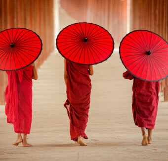 3 personnes marchant de dos portant des habits traditionnels avec des parapluies rouges
