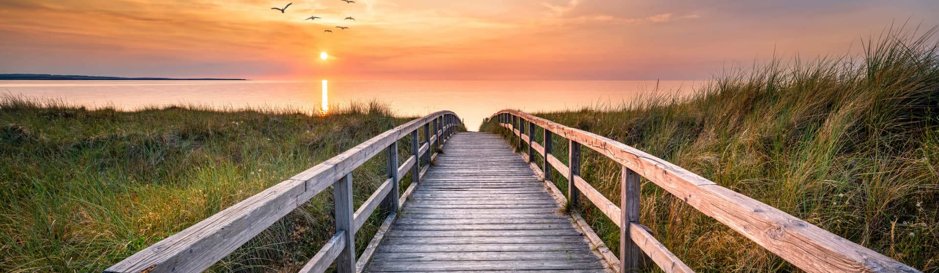 photographie d'un long pont avec vue sur un coucher de soleil orangé et la mer