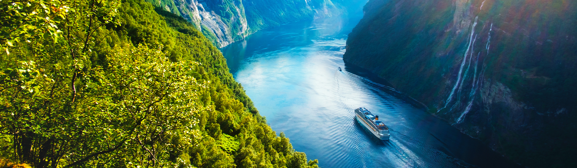 image d'un bateau de croisière passant entre deux montagnes dans le village de Geiranger, remplie de verdure et de hauteur donnant vue sur les chutes d'eau Seven Sisters