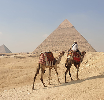 image d'un homme en chameau devant une des trois grandes pyramides de Gizeh en Egypte