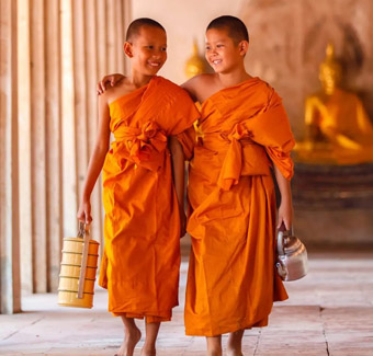 image de 2 jeunes garçons moines bouddhistes se tenant par l'épaule dans un temple en portant une tenue traditionnelles : des robes orange