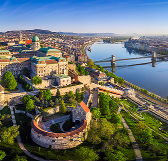 image avec une vue panoramique aérienne du Palais Royal de Buda avec le pont de la Chaîne Szechenyi, la basilique Saint-Étienne, le Parlement hongrois et l'église Matthias au lever du soleil