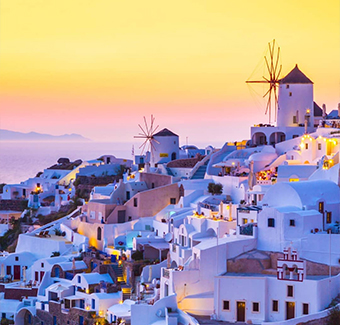 image de l'île de Santorin avec ses maisons blanches et bleues au sommet des falaises lors d'un coucher de soleil