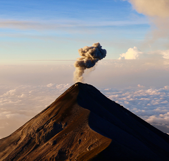 image du volcan Fuego qui éructe de la fumée dans le ciel bleu au-dessus des nuages du matin au Guatemala