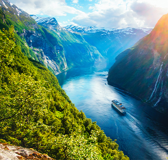 image d'un bateau de croisière passant entre deux montagnes dans le village de Geiranger, remplie de verdure et de hauteur donnant vue sur les chutes d'eau Seven Sisters