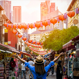 image d'une femme au premier plan de l'image levant les bras en l'air de joie devant le quartier chinois à Singapour