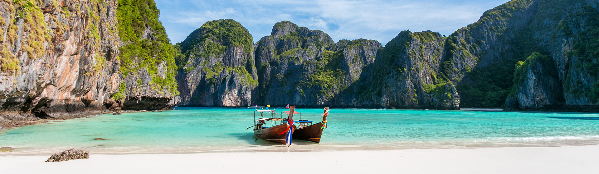 image d'une vue panoramique sur la baie de Maya sur l'île de Phi Phi Leh avec 2 longs bateaux garé surplombant la plage de sable blanc, l'eau claire et le beau ciel