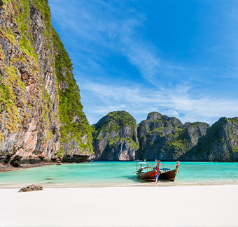 image d'une vue panoramique sur la baie de Maya sur l'île de Phi Phi Leh avec 2 longs bateaux garé surplombant la plage de sable blanc, l'eau claire et le beau ciel