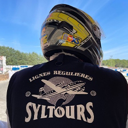 image d'un homme de dos avec un casque de karting et un teeshirt noir personnalisé avec un avion et le nom de l'enseigne syltours