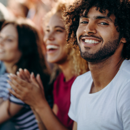 image d'un homme brun à cheveux bouclés souriant à la caméra et d'une femme blonde avec des cheveux bouclé également regardant devant elle et applaudissant avec d'autres