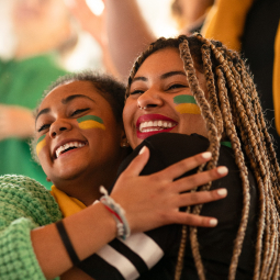image de 2 jeunes filles se prenant dans les bras avec le drapeau du brésil dessiné sous forme de maquillage sur leurs joues